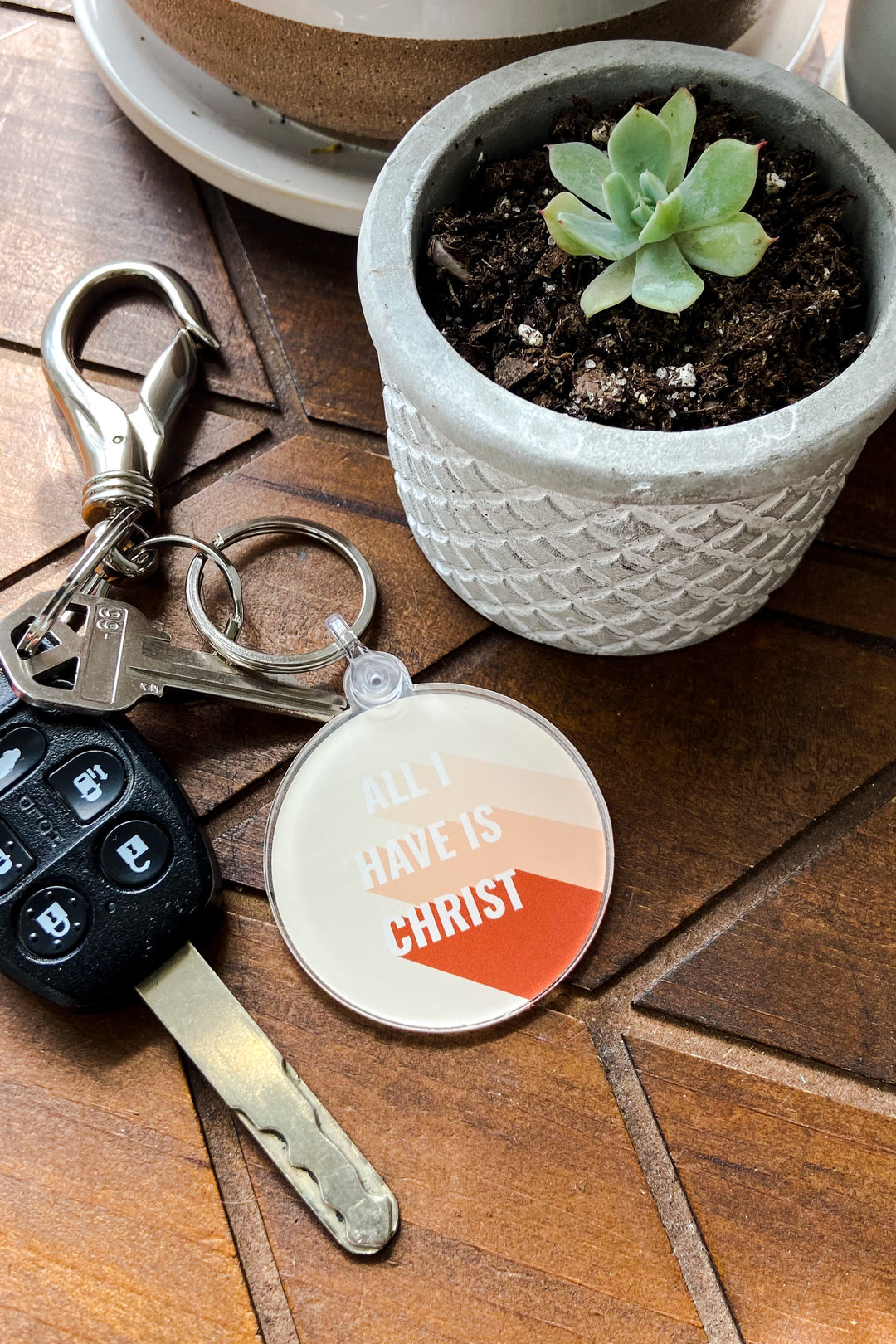 keychain that says, "All I have is Christ" sits on a table next to a potted plant